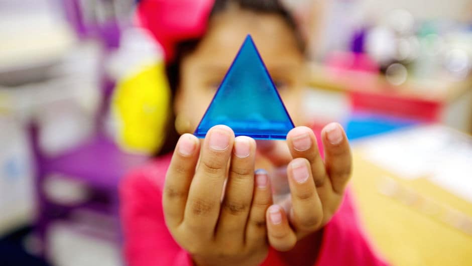 A young student holding a small clear blue pyramid.