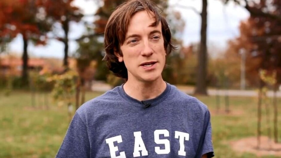 A man stands outside wearing a blue shirt that says EAST