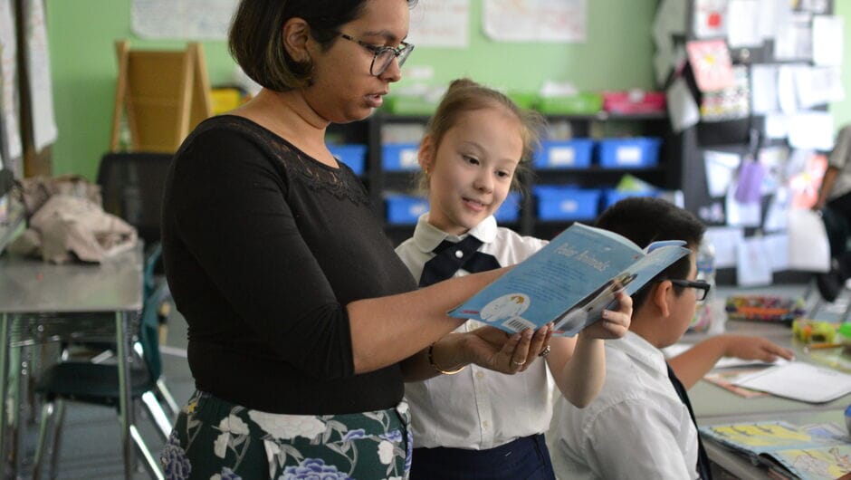 A female teacher looks at a book with her student.
